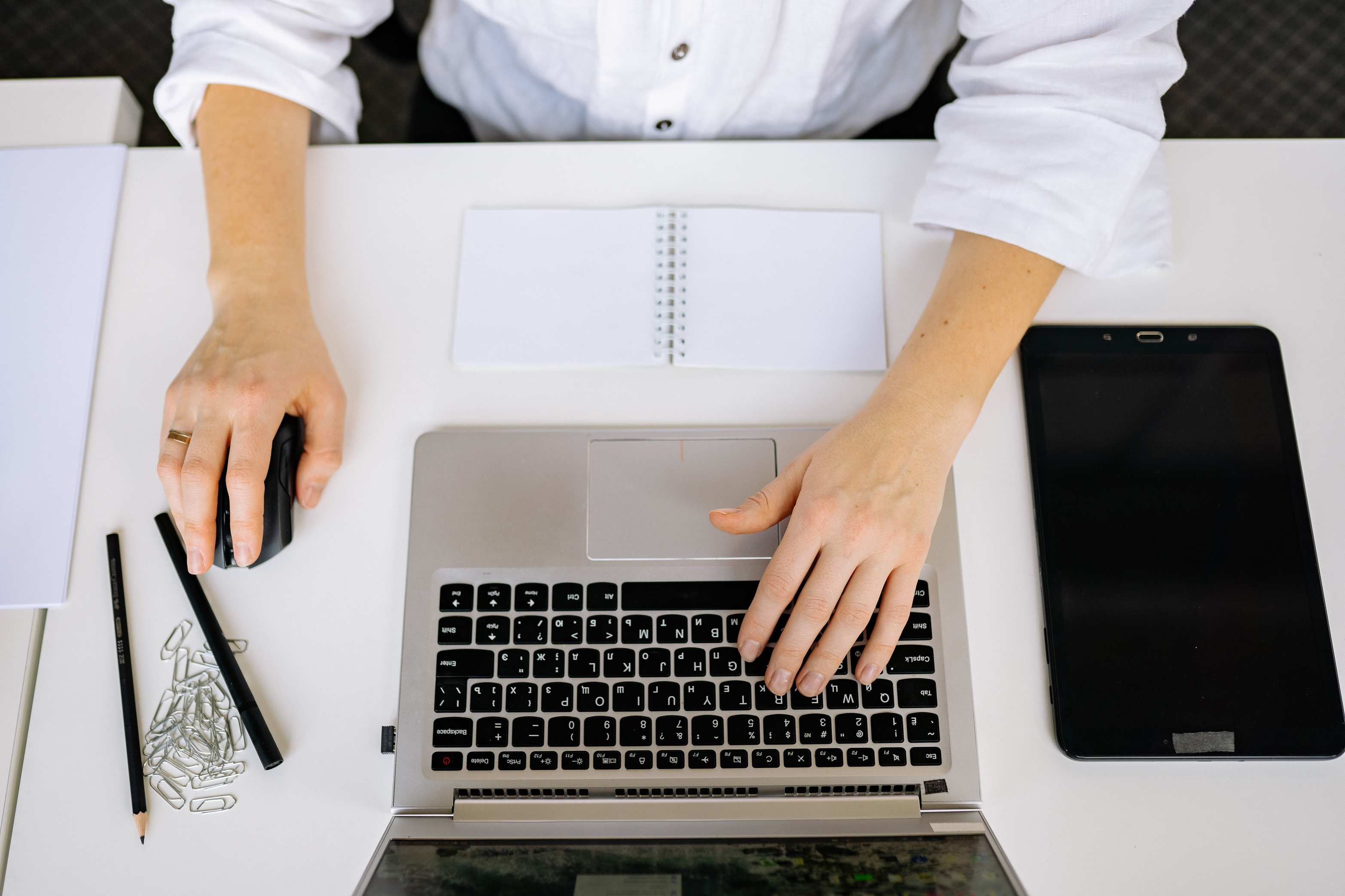 Top view of an office workspace with a laptop, tablet, and hands typing
